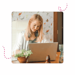 A woman sitting at a table in front of a laptop whilst smiling.