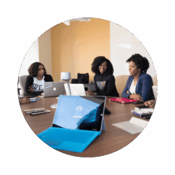 3 women sitting at a desk attending a meeting. 2 of the women have their laptop open, but the woman on the right has hers closed. There is also an open 